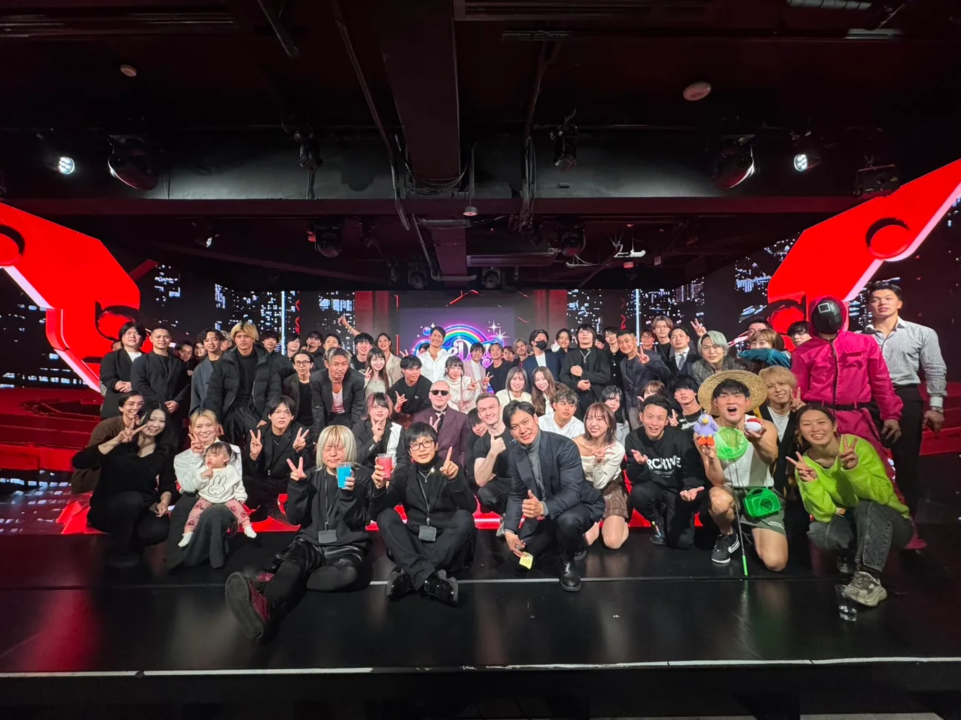 赤い照明のクラブ会場で撮影された大人数の集合写真
